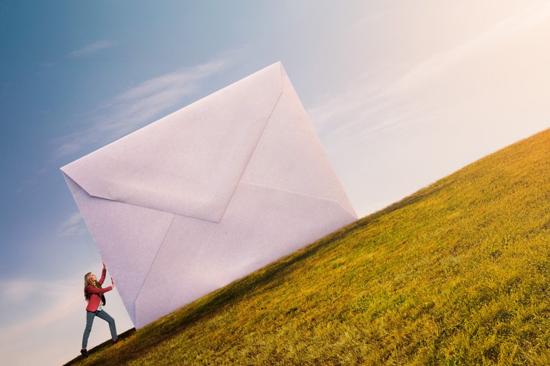 Person pushing a giant envelope up a hill